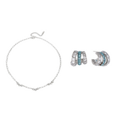 A jewelry set featuring a delicate silver chain bracelet and matching silver huggie hoop earrings, both adorned with small light blue stones, displayed on a clean white background.