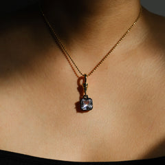 A gold chain necklace with a square-cut dark purple gemstone pendant